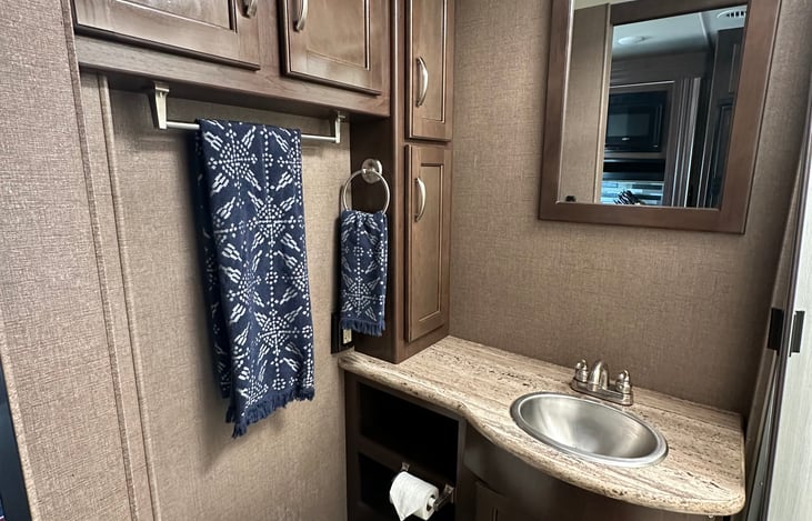 Bathroom with step flush toilet, sink, storage, and shower with hot water