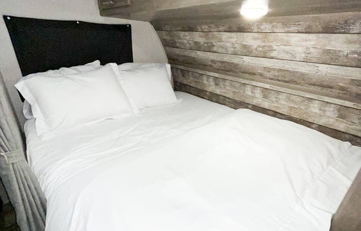 Queen bed in the main part of the camper! Half wall and curtain for privacy. Cabinets above and to the right with a bar for hanging clothes.