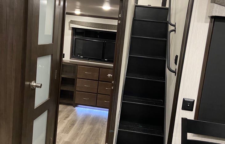 Stairs to life, pantry and rear bedroom / lounge equipped with a desk area, dresser and tv.