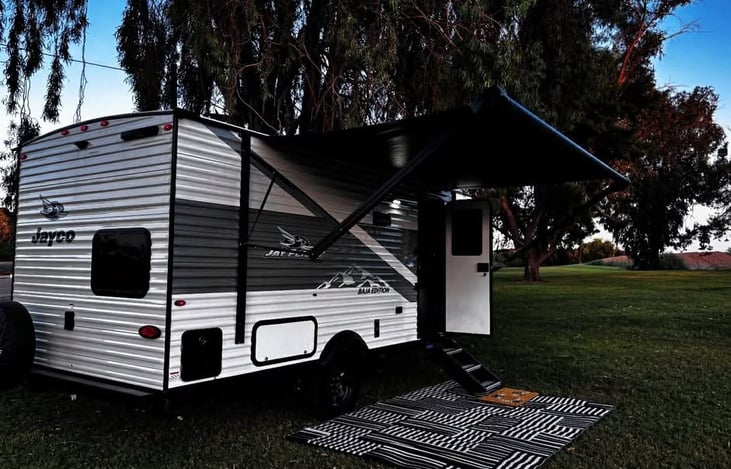 A clean, modern Jayco trailer set up under the awning with an outdoor mat, ready for relaxing at your campsite.