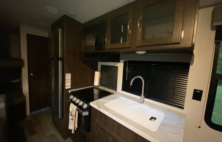 Kitchen area, huge refrigerator and freezer, gas stove, and full sized sink.  A cutting board covers  the sink to create more counter space.