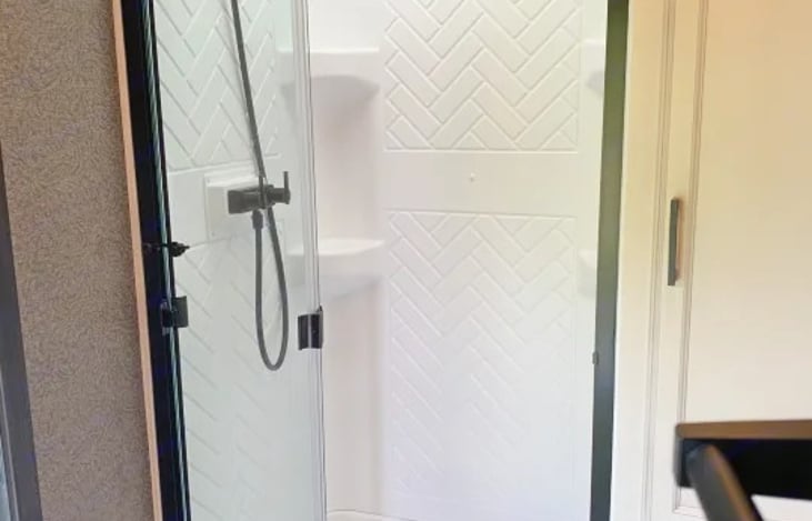 Full bath includes a modern radius shower with ample headroom (comfortable for individuals up to 6'5"), a foot-flush toilet, a medicine cabinet, and a dedicated toiletries closet