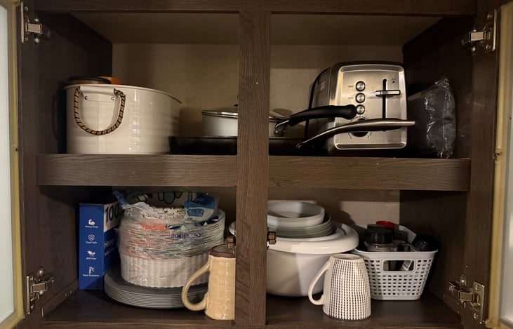 Kitchen cabinet with plates, cups, bowls, skillet, small pot, toaster, mixing bowls, and two mugs.