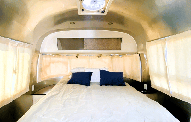 Front private bedroom with panoramic Airstream windows. Bright, quiet space with a comfortable queen bed and natural light on both sides. A calm, cozy setup for restful nights on the road.