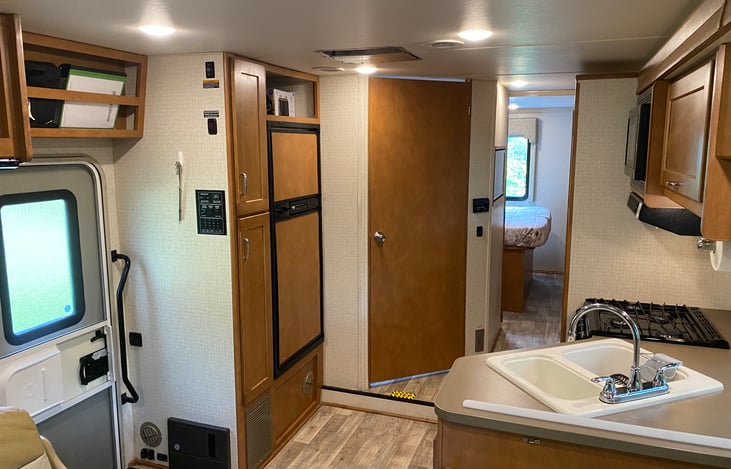 Kitchen area with dual power fridge, 3 burner stove, & double sink. Bathroom door and hallway to bedroom.