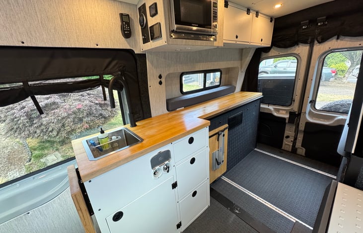 Cook like a chef wherever you park with a full countertop, deep sink with filtered water, induction cooktop, microwave, and smart storage. Rugged, modern, and ready for off-grid van life.
