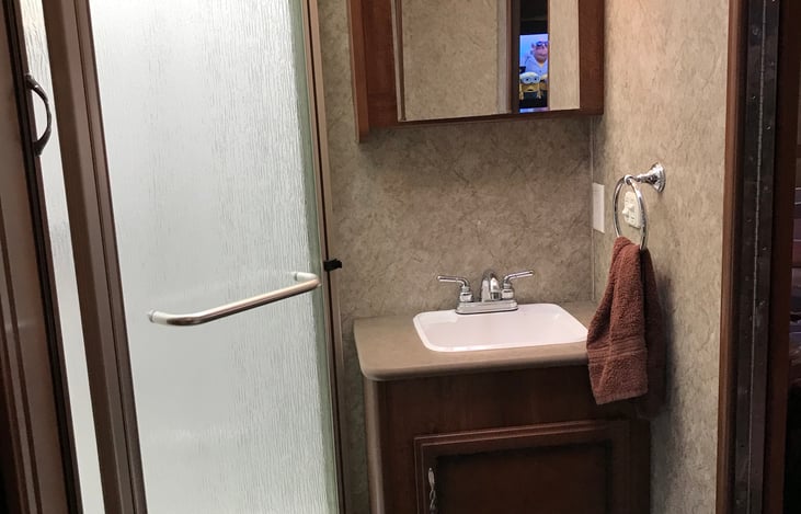 Bathroom with sink, medicine cabinet and corner shower with glass door.