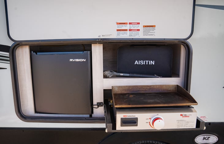outdoor kitchen features a flat top grill and mini fridge.