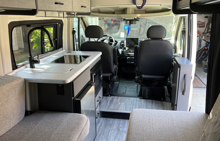 BEAUTIFUL VIEW OF KITCHEN WITH FIDGE AT BOTTOM OF SINK WITH TWO FRONT SWIVEL SEATS IN THE BACKGROUND