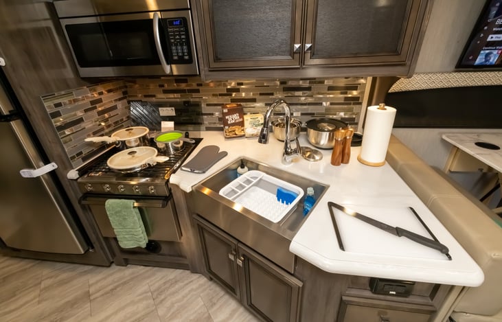 Fully equipped kitchen with mixing bowls, pots and pans, pasta strainer, cutting boards, chef's knife, dish drying rack
