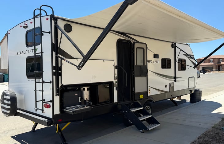 Outdoor kitchen equipment with a mini fridge, small grill, stove top, air fryer, outdoor shower and BBQ utensils. Long awning with LED lights. Chairs and table  stored in the pass-through  storage.