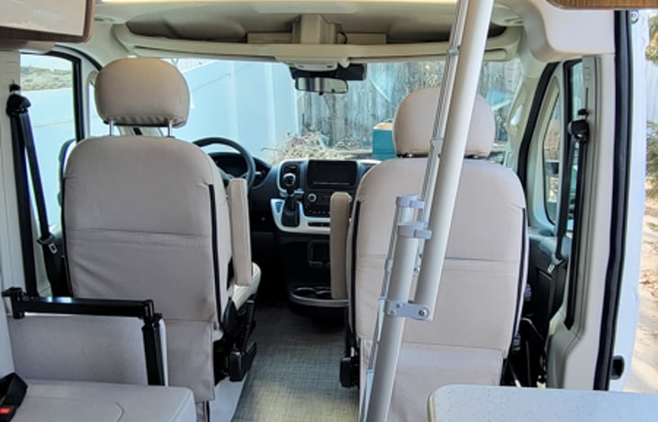 Front of van with ladder to sky bunk and two seats to the left with two more seatbelts.