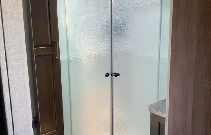 "Micro Easy" showcases a large radius corner shower protected by a frosted glass door, employs the Showermiser Water Saving System,