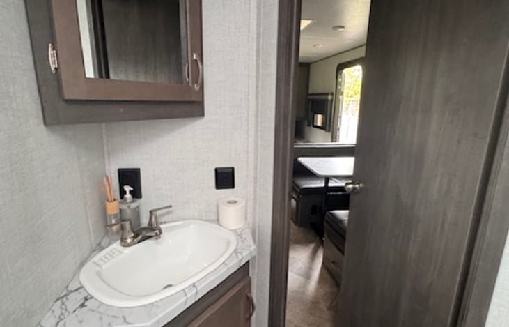 Perfect sized sink and lower storage cabinet, stocked with toilet paper and hand soap