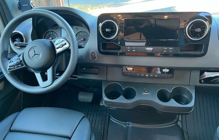 Get ready to hit the road in style! The driver’s side of our 2022 Mercedes-Benz Sprinter campervan is equipped with modern features for a smooth and comfortable journey.