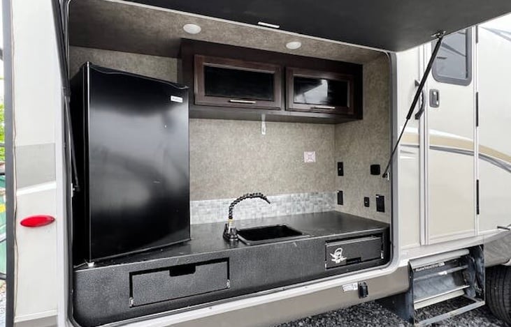 Outdoor kitchen with storage drawer & cabinets, grill, refrigerator, and sink.