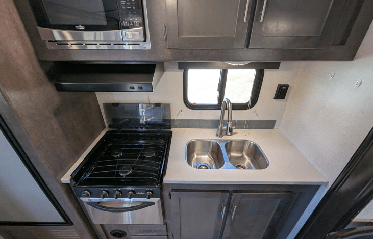 Well-equipped kitchen featuring expansive solid-surface countertops, a stainless steel microwave, oven, and a glass-top range, this layout offers significantly more meal-prep space than traditional mi