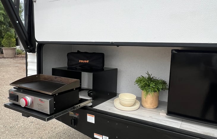 outdoor kitchen with flat top griddle, cooking tools, and mini fridge