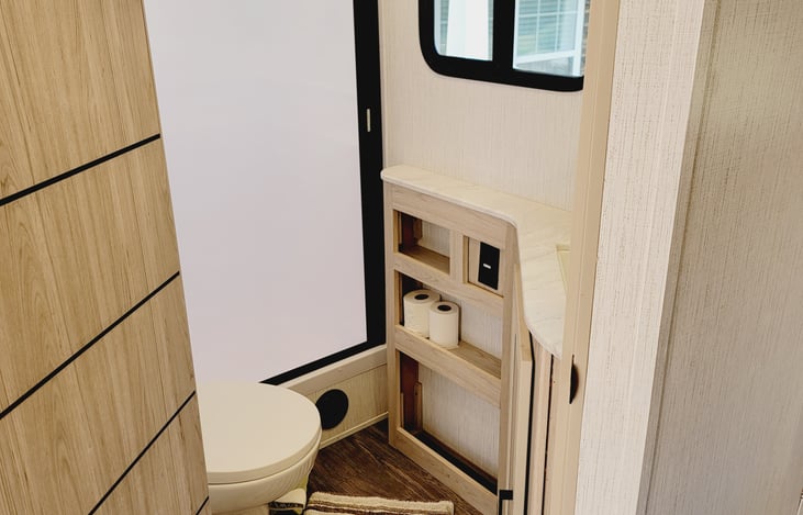 Bathroom with toilet, shower, mirror, sink, exhaust fan and natural light.