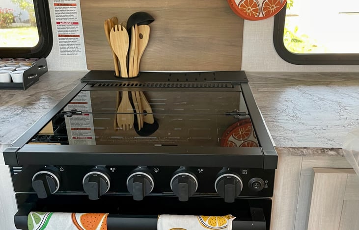 There is 2 hot pot holders, cutting board above the stove, the glass over the stove pulls up & back, there is 4 towels available and kitchen utensils.