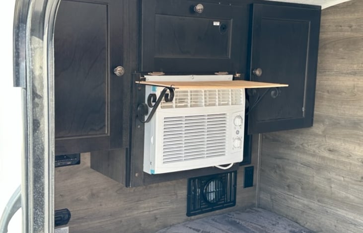 Cabinets and shelf above the bed with air conditioner and heater vent at foot of bed