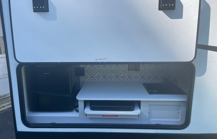 Outdoor Kitchen includes sink with hot and cold water, two burner stove, and mini fridge. There is also an electrical outlet for additional devices.