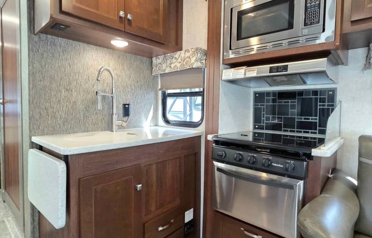 Fully equipped RV kitchen featuring a sink, microwave, 3-burner stove, oven, countertop space, storage cabinets, and backsplash—everything you need to prepare and enjoy meals during your stay.