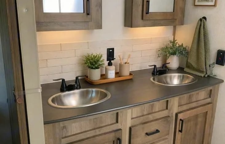 A walk-through bathroom is positioned between the kitchen and bedroom, this large bathroom features a dual-sink vanity, two medicine cabinets, a porcelain foot-flush toilet, and a glass radius shower