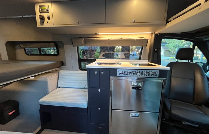 Sink, induction cooktop, refrigerator, plates, bowls, cookware, silverware, and utensils are clean and ready for travel.