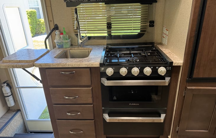 Counter area with burner cover raised, stainless steel sink, counter extension  raised and sink opening cover on the extension