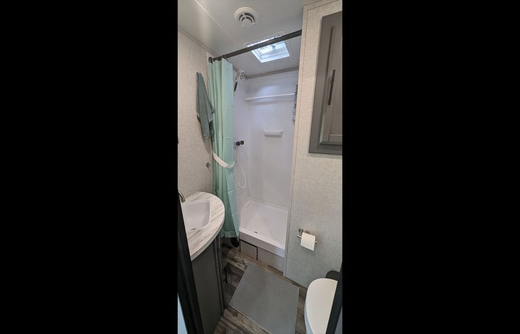 Light filled bathroom with shower stall, roof vent, sink and toilet.