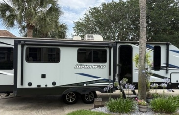 Right side exterior. Entry door with both sunshade retracted. Storage compartment in the front. two exterior speakers and TV mount on right side as well.