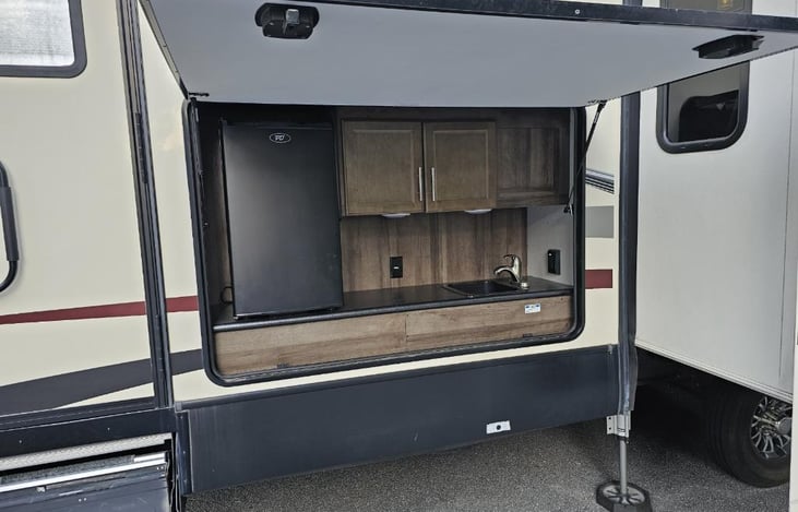 Outdoor kitchen area with mini fridge and sink with cabinets.