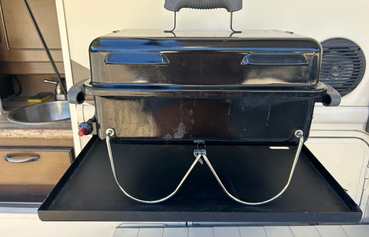 A gas bbq and metal shelf are stored in an outdoor storage locker.