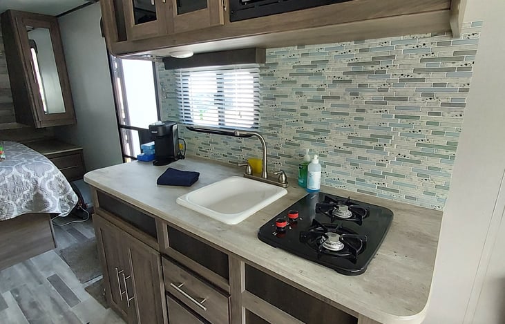 the fully stocked kitchen features a Two burner stove, Deep sink, toaster, Microwave and Kuerig style coffee maker.  Dishes, utensils, coffee mugs and wine glasses are all ready for filling.