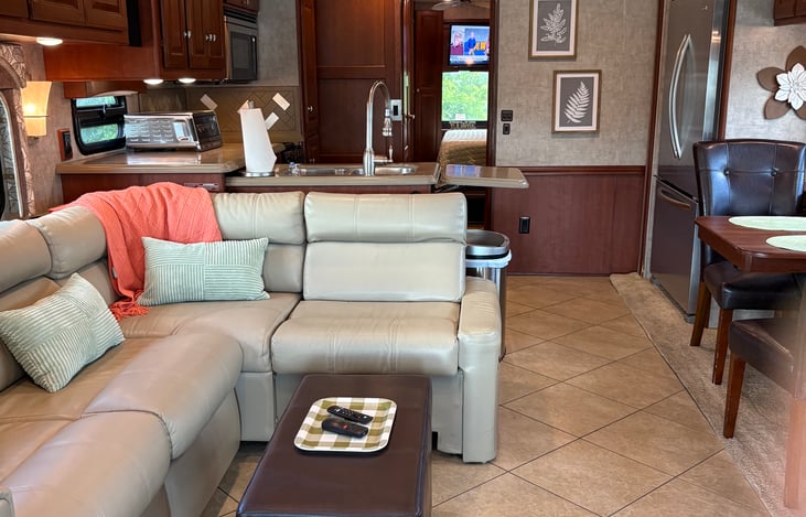 Reclining sofa and ottoman. Kitchen has a microwave, stove top, air fryer, pantry and residential fridge. The bathroom is split with a toilet on one side and shower on the other.