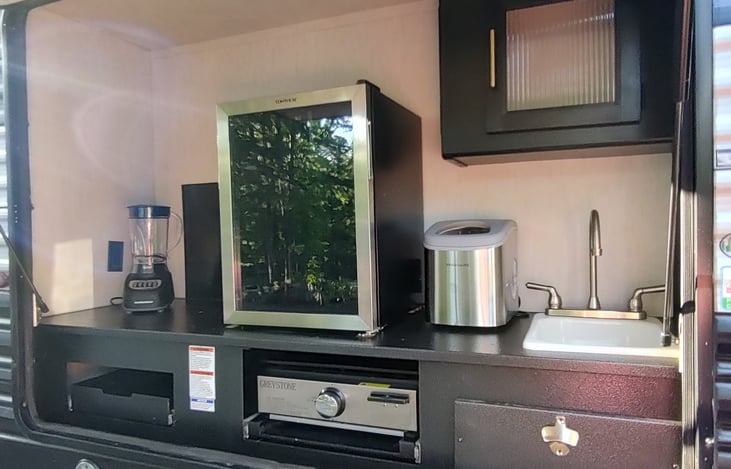 Outdoor kitchen with mini fridge, grill, sink, icemaker and blender.
