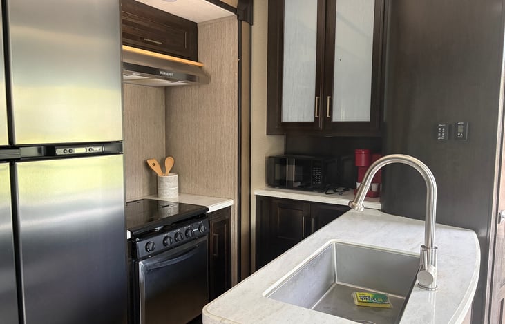 Kitchen with full refrigerator with freezer, stovetop, oven, microwave and keurig for coffee maker.