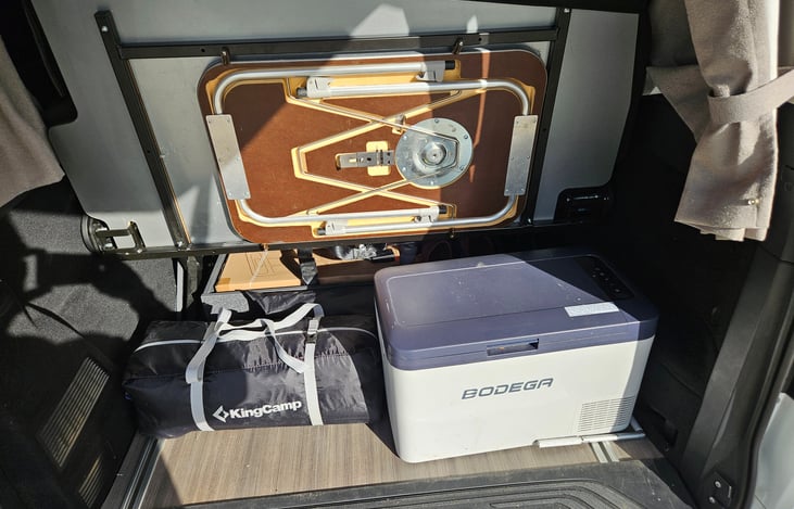 Back hatch open. Fridge on right. Tent on left. Table above.