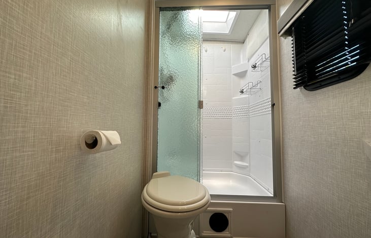Porcelain toilet and full shower with residential shower head. Lots of storage shelves and hooks as well