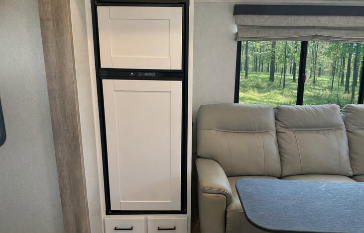 12V residential-style refrigerator with lower storage drawers and adjacent seating area. Energy efficient and spacious for extended stays.