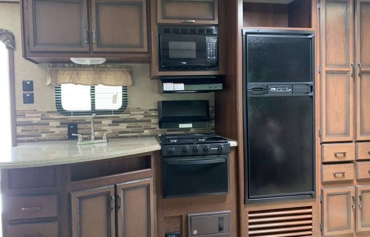 Kitchen with double sink, freezer, refrigerator, microwave, vent, gas stove, gas oven, dishes, cutlery, serving ware, cookware, and storage.