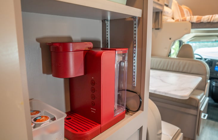 Keurig coffee maker with selection of coffees, creamer, and sugars included.
