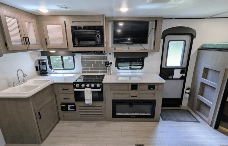 Spacious and cozy interior with well-equipped kitchen, large refrigerator, ample counter space, electric fireplace, TV, stereo, and bunks.