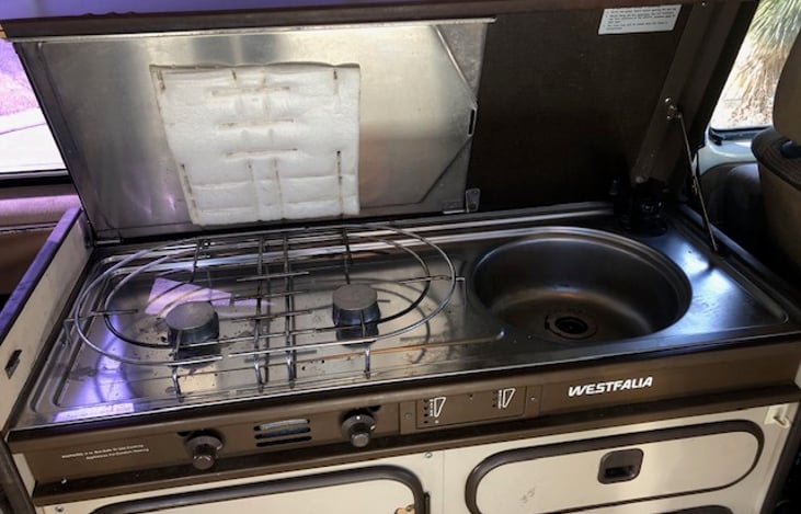 Cook station with 2-burner propane stove and sink.  Water delivered to sink from on-board reservoir by electric pump.  Metal draining board can be lowered onto stove top when doing dishes.