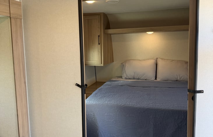 Restful master bedroom suite equipped with a comfortable queen bed, overhead storage cabinets, and warm ambient accent lighting.