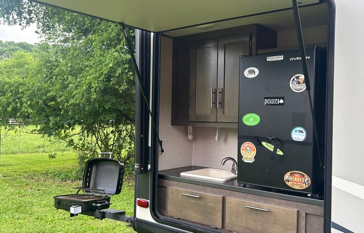 Outdoor Kitchen with Mini Fridge, Sink, and storage space and gas grill attaches to arm on side.