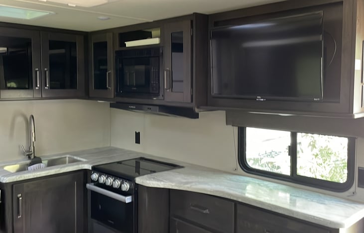 Counter top extender next to sink. Large refrigerator and freezer. Stocked with kitchen gadgets, utensils, cups, plates, bowls, cookware and spices.