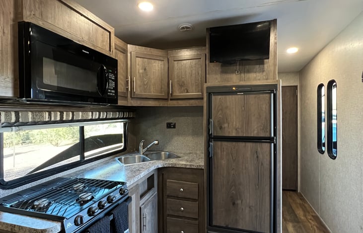 Kitchen features 3-burner range with thermostatically controlled oven, dual bowl sink with removable spray  faucet, overhead storage, below counter drawers and two-zone refrigerator freezer.