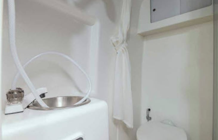 Bathroom with sink shower and toilet.  There is peddle next to toilet for flushing. Cabinet above to store bathroom items.